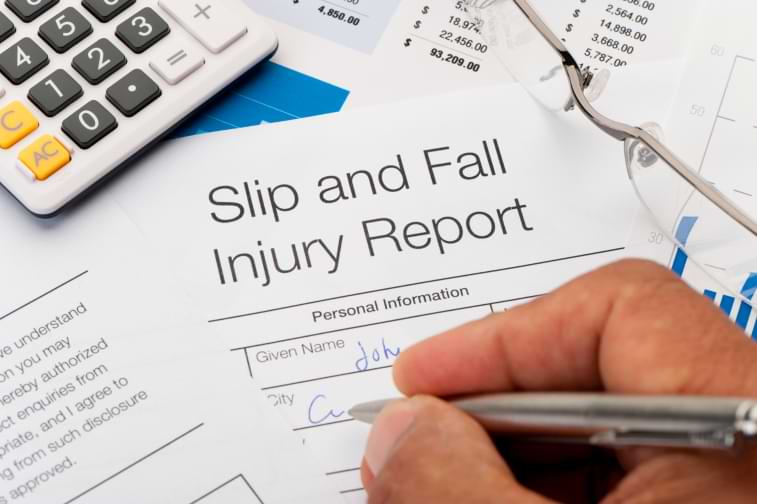 A hand is shown filling out slip and fall injury claim form surrounded by papers and a calculator 
