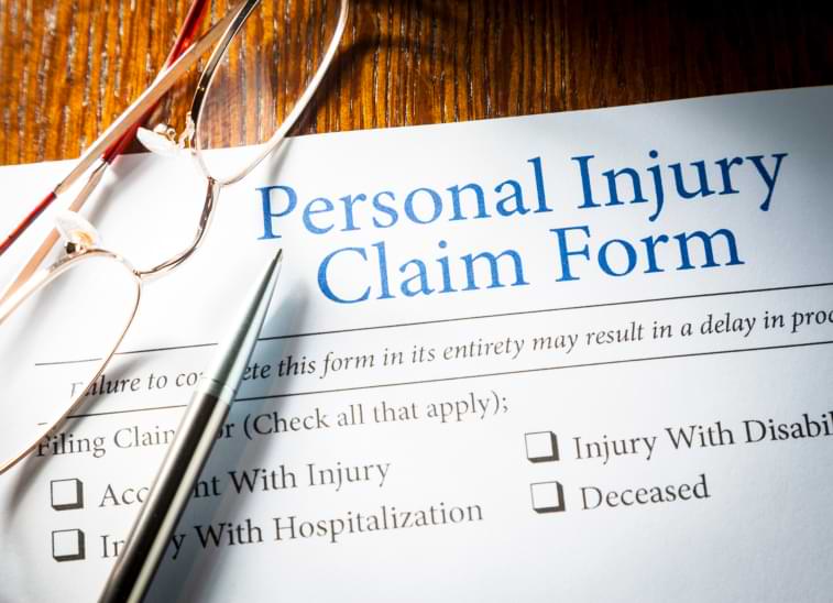 A pair of eyeglasses and a pen lay on top of a personal injury claim form on desk